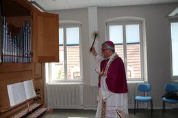 Bischof Wiesemann mit einem Weihwasser-Wedel in der Hand segnet eine Orgel im neuen Haus der Kirchenmusik in Speyer.